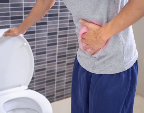 A picture of a male leaving the bathroom after he used the toilet that is in the background, while holding his stomach in pain.