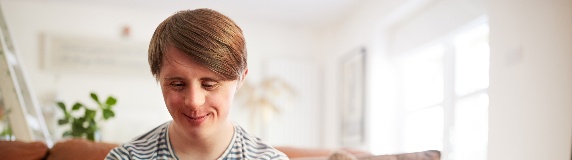 Teenager sitting on couch looking down and smiling sweetly.