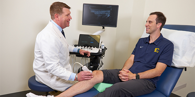 Provider performing ultrasound on patient's knee in clinic.