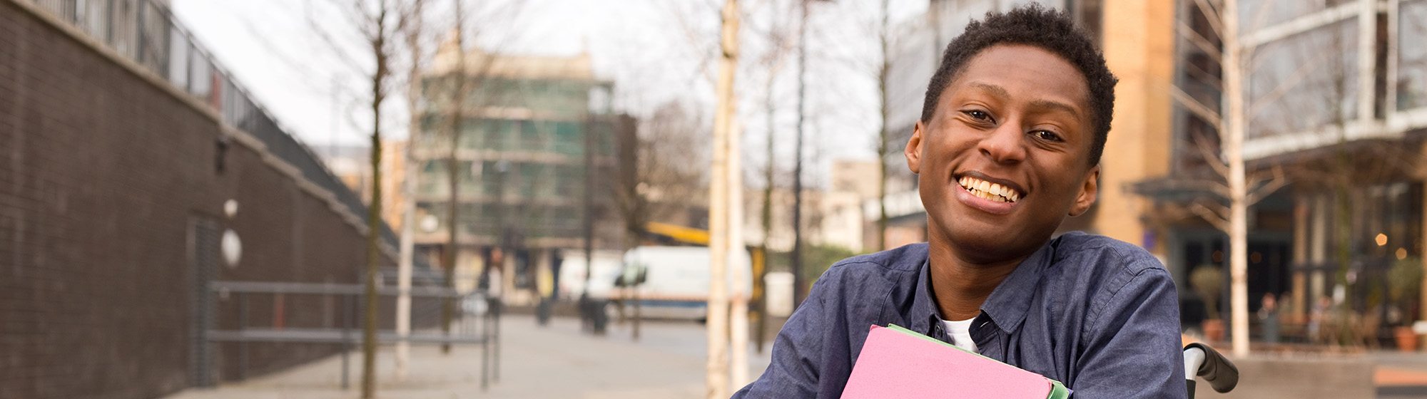 Teenager in a wheelchair holding a folder smiling at the camera.