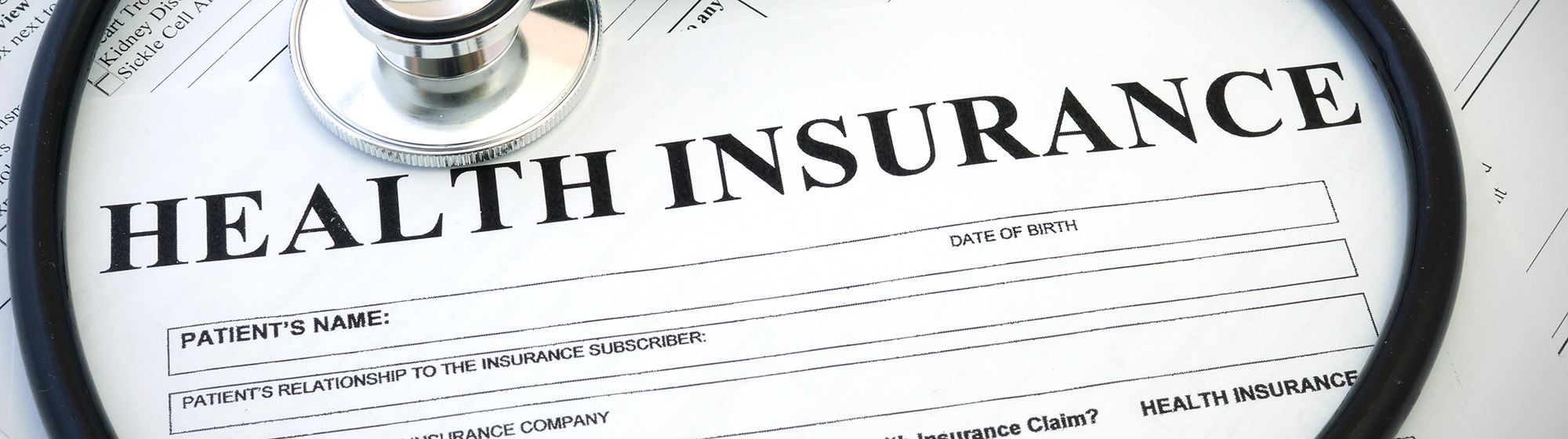 Paperwork titled health insurance with a stethoscope laying on top. 
